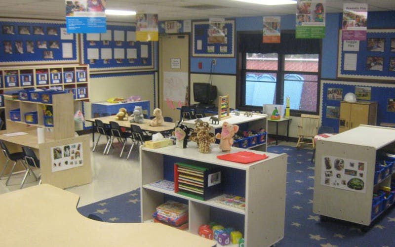 Classroom with small tables, chairs, shelves with toys, and posters on blue walls