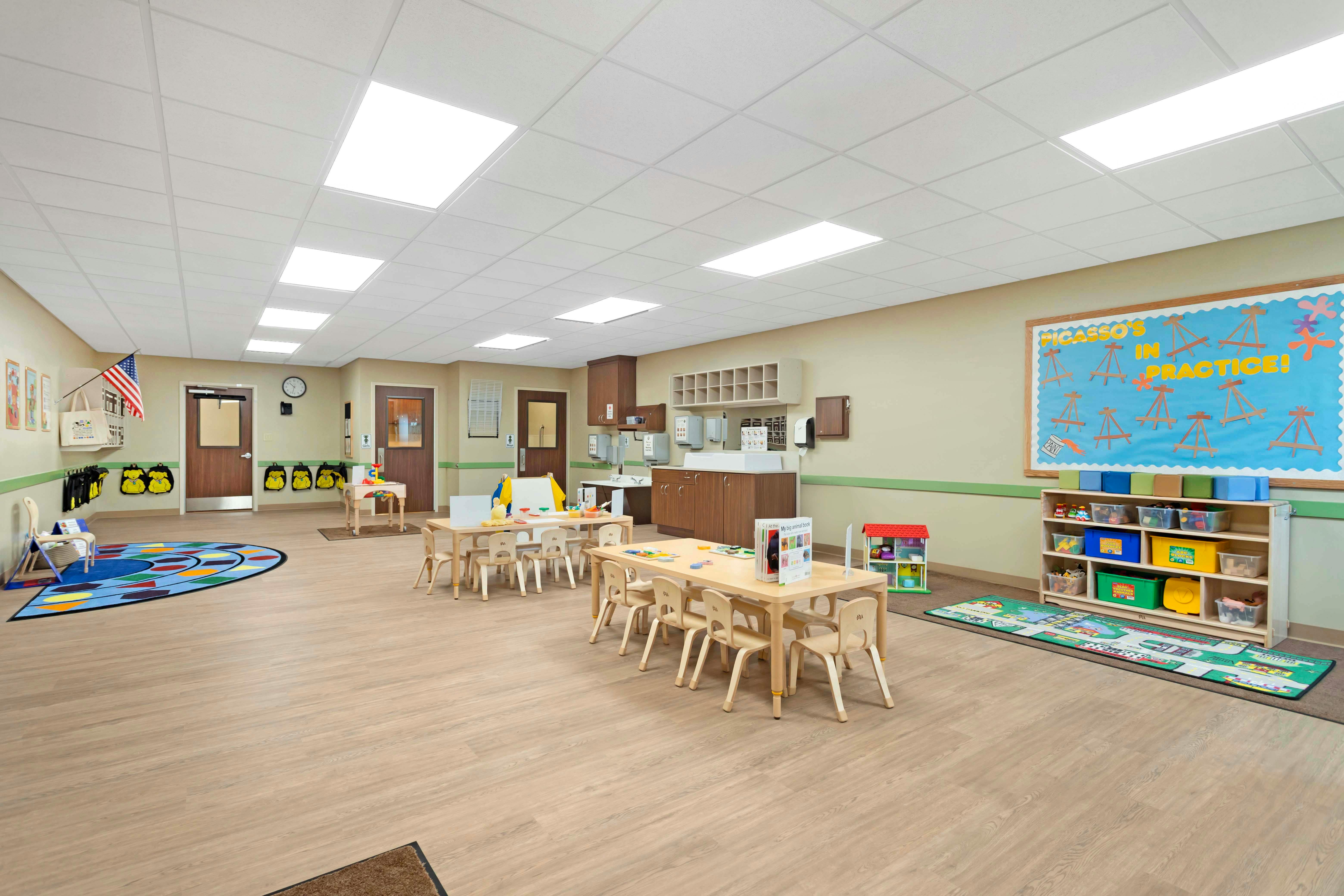 An empty classroom with multiple small tables, chairs, and play areas