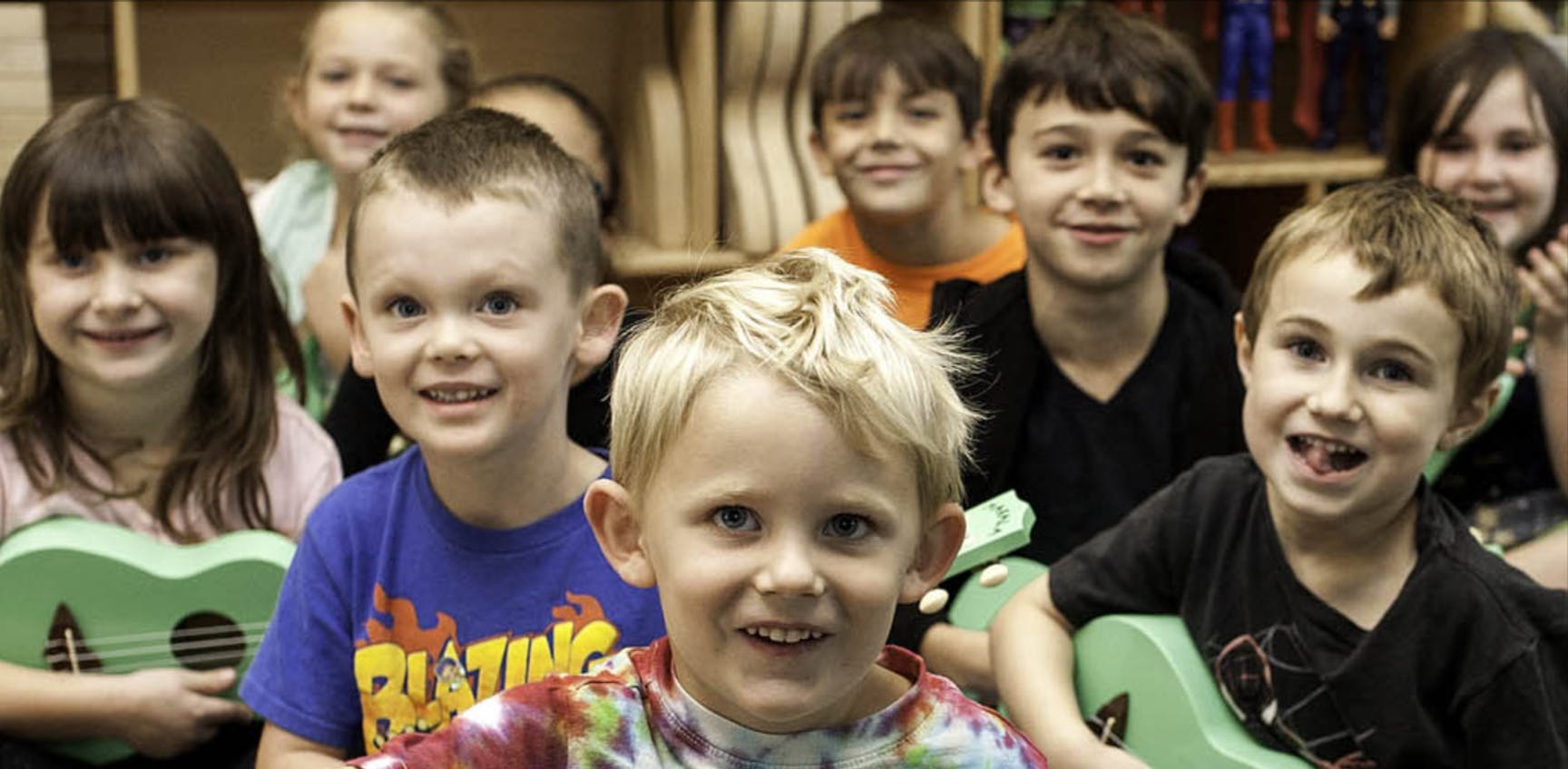 Group of children smiling, some holding small guitars