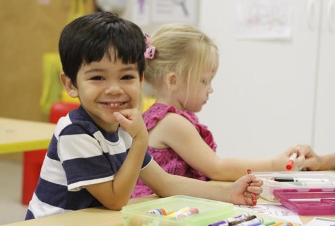 Child smiling at a table with another child drawing