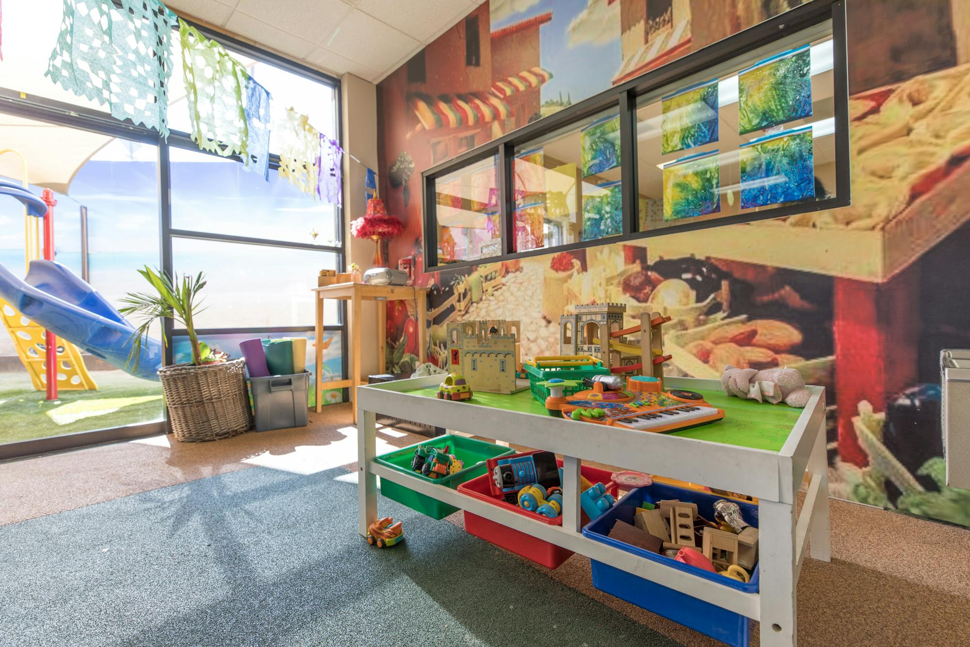 Playroom with a toy table, storage bins, and a slide visible through a window