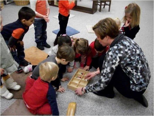 Adult and children gathered around a wooden tray with compartments