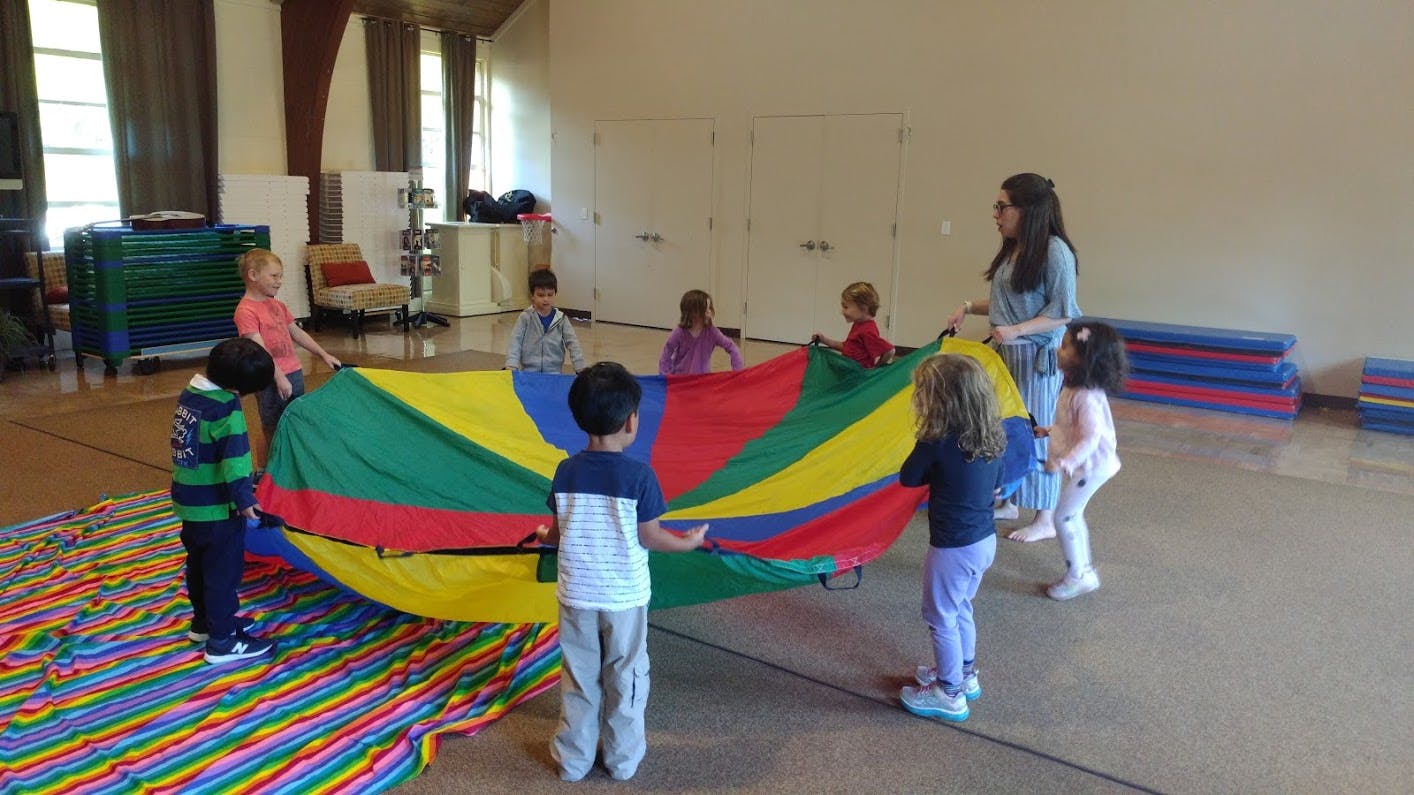 Children and an adult playing with a colorful parachute