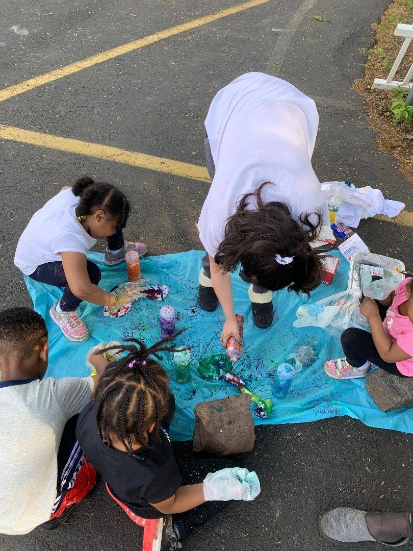 Adult and children doing an art activity on a blue tarp outdoors