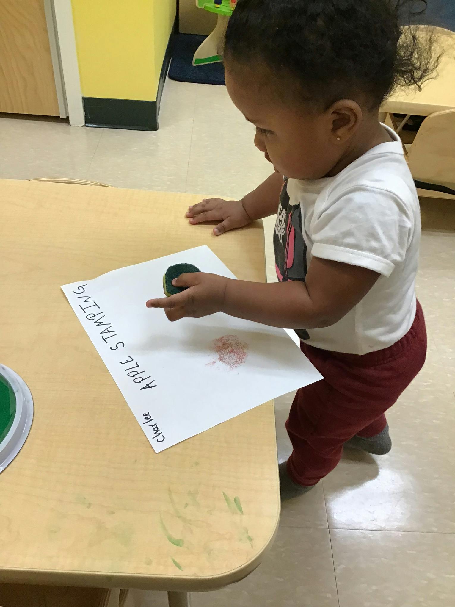 Child stamping on paper with "Apple Stamping" written on it