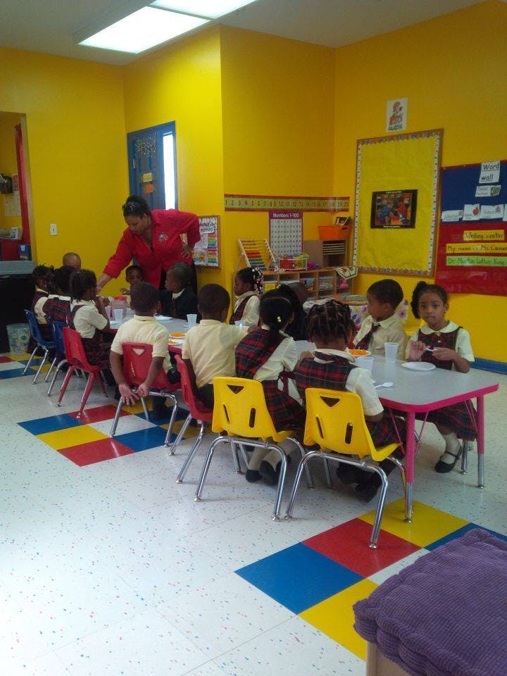 Adult helping children seated at tables in a classroom