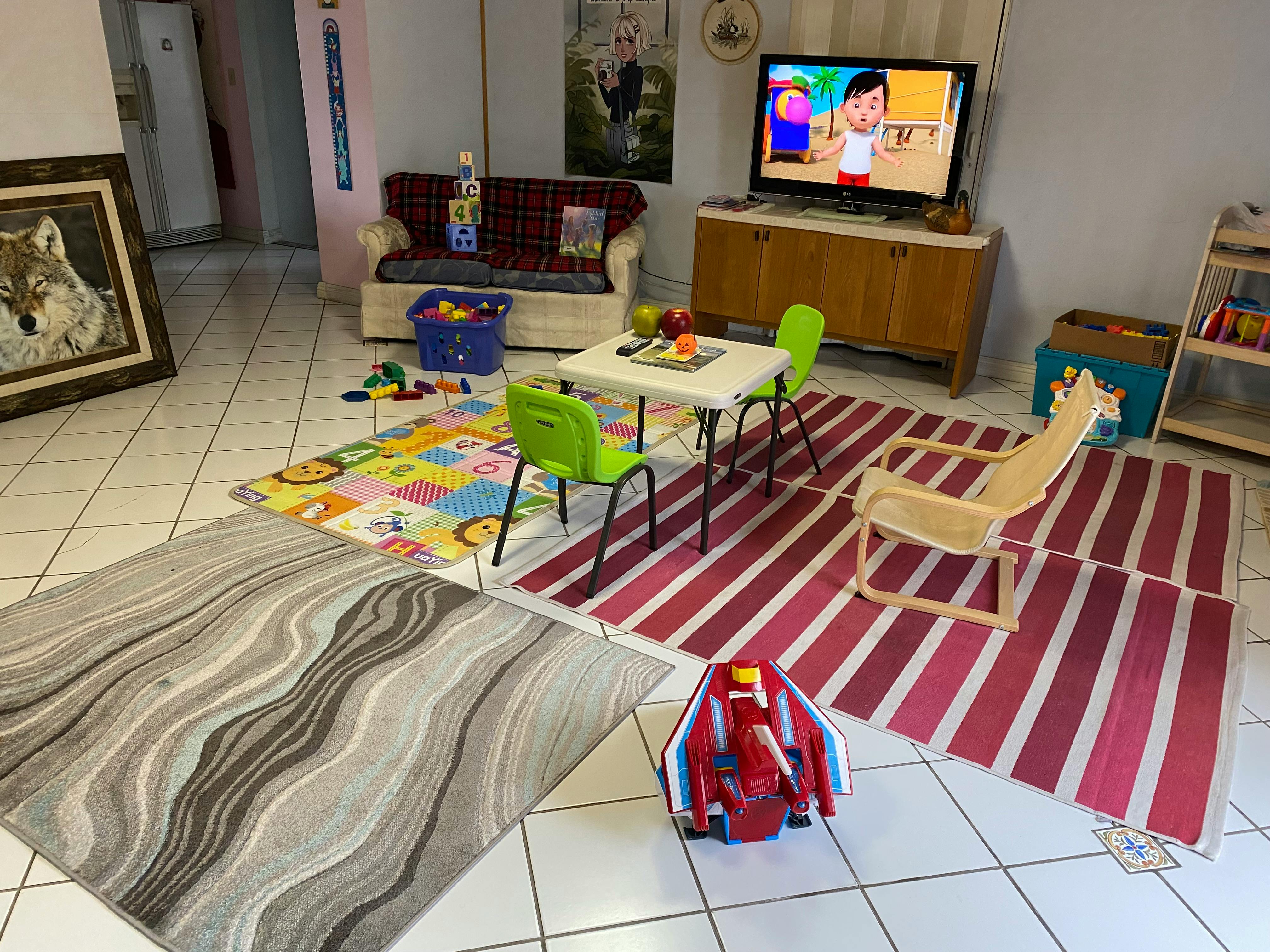 Living room with multiple rugs, a small table with chairs, and a television