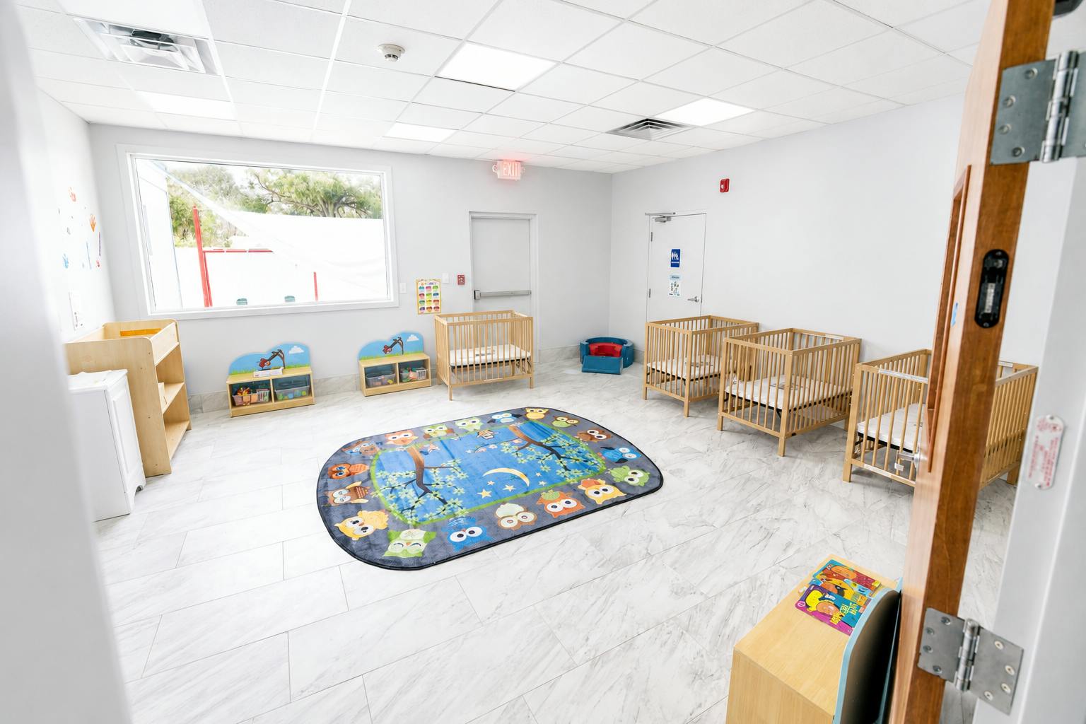 Childcare room with multiple cribs and an owl pattern rug on the floor