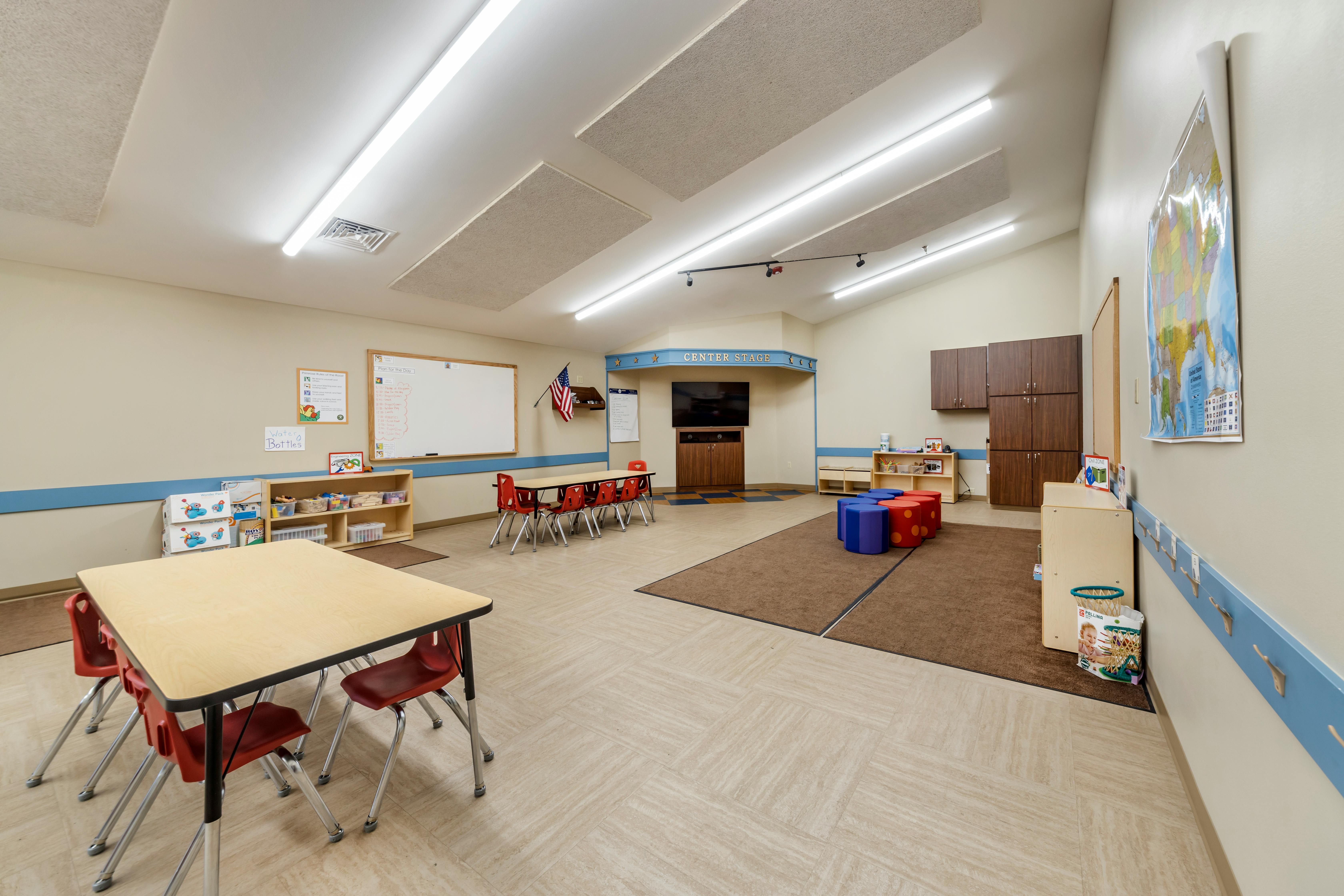 Classroom with child-sized tables and chairs, a stage, and play area