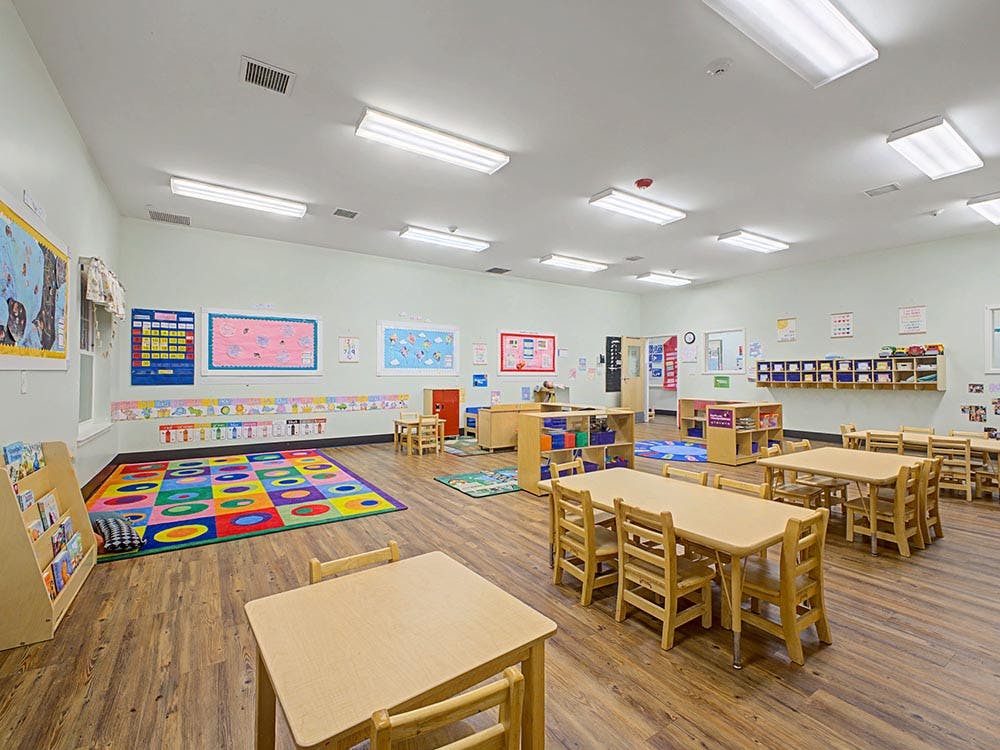 Classroom with small tables and chairs, colorful rug, and decorated walls