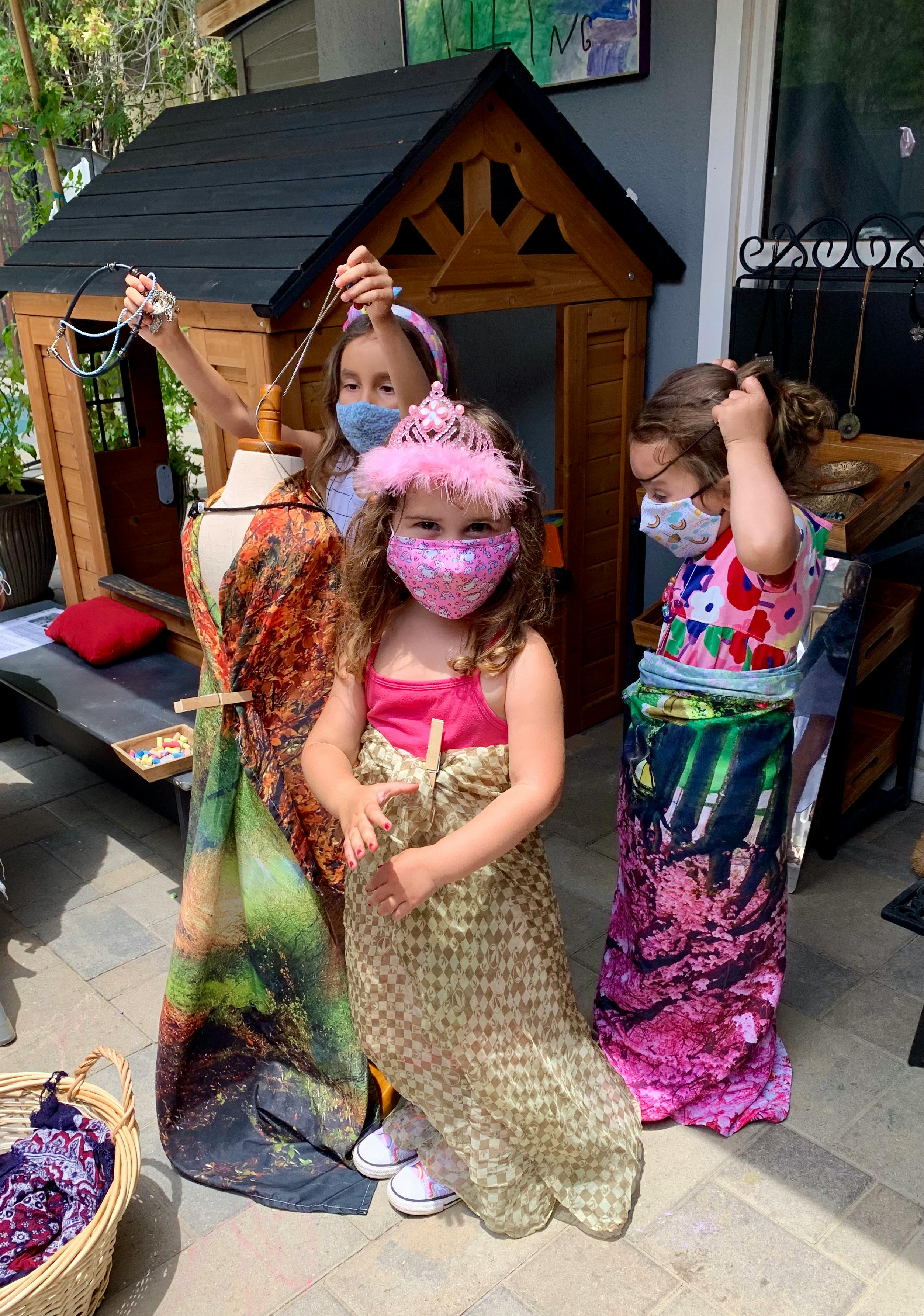 Three children in face masks playing dress-up with colorful fabrics
