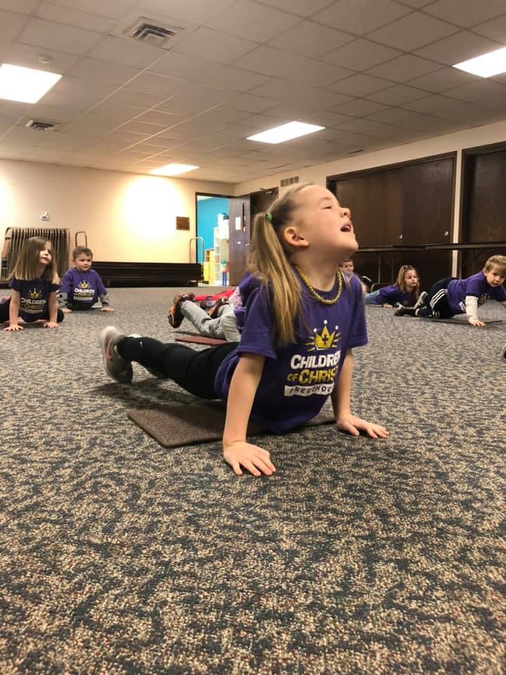 Child in purple shirt doing a yoga pose on a mat with other children