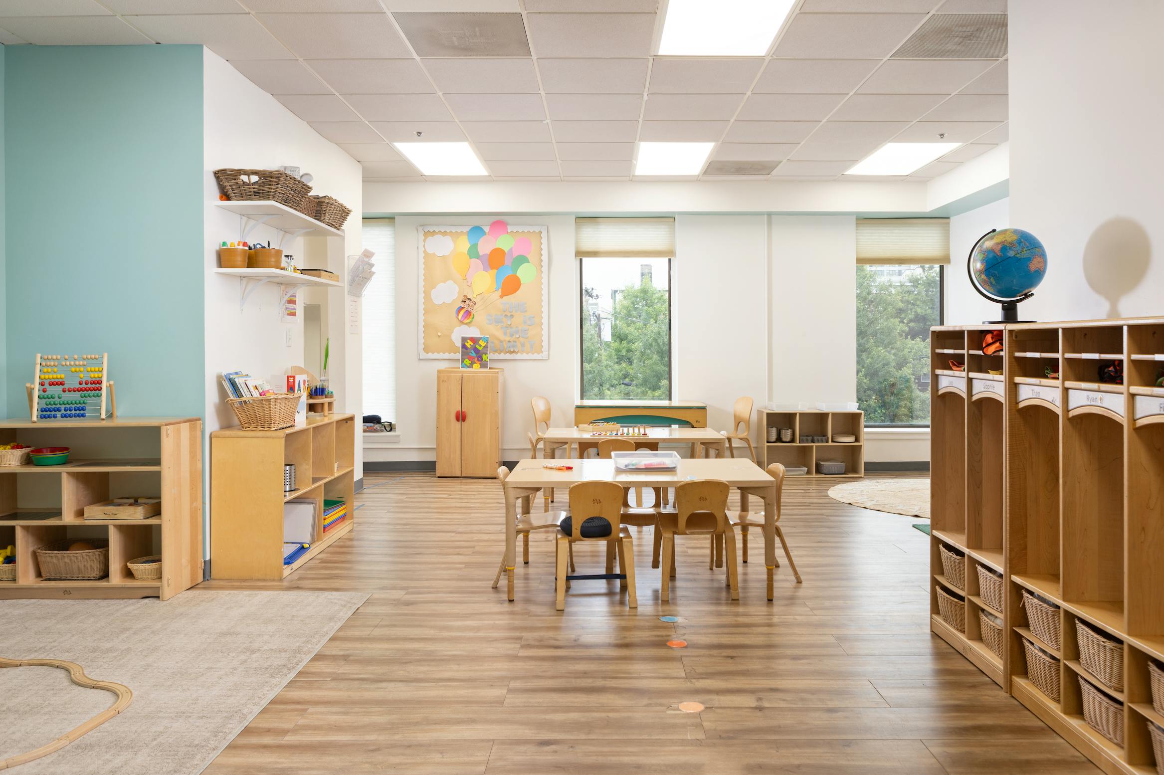 Empty classroom with small tables and chairs, shelves, and windows