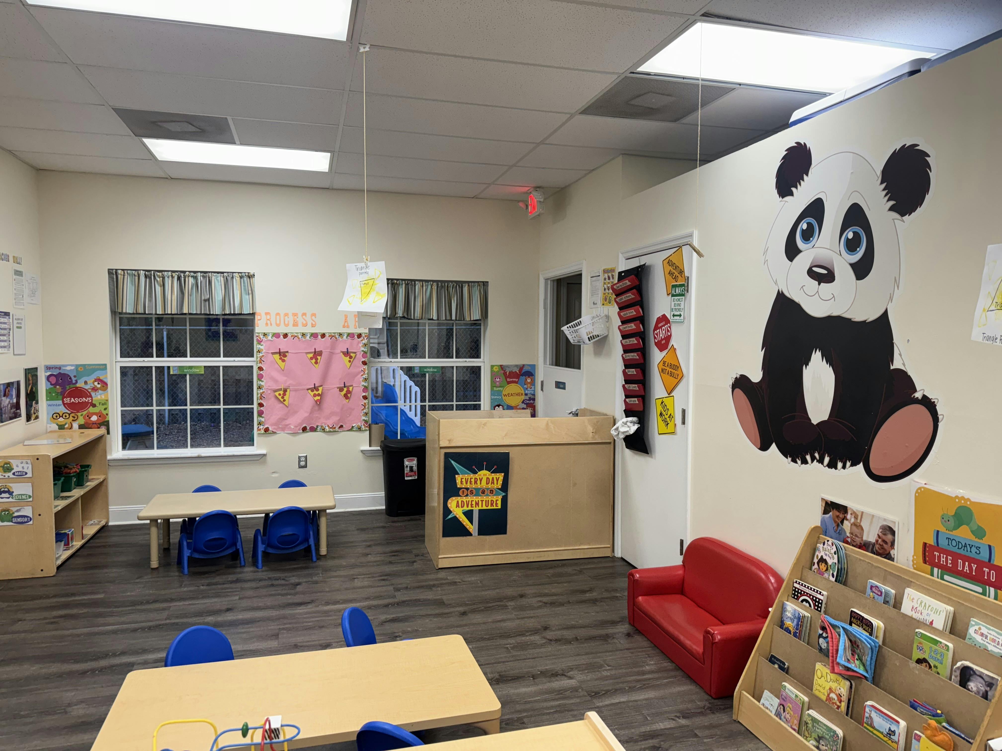 Classroom with small tables and chairs, a panda wall decal, and a red couch