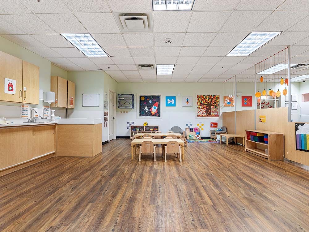 Classroom with small tables and chairs, artwork on walls, and a sink counter