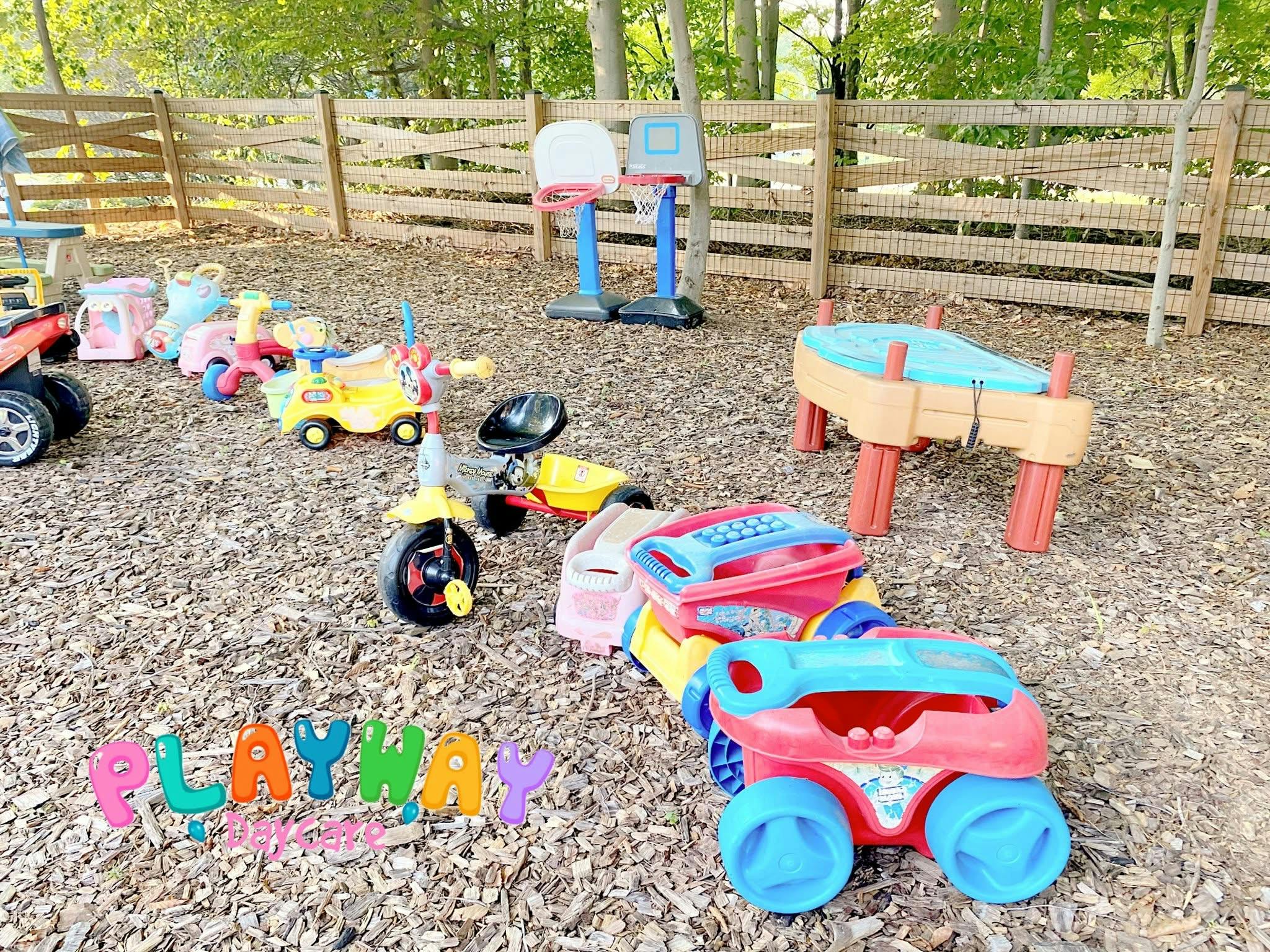 Outdoor play area with various colorful ride-on toys and a sand table