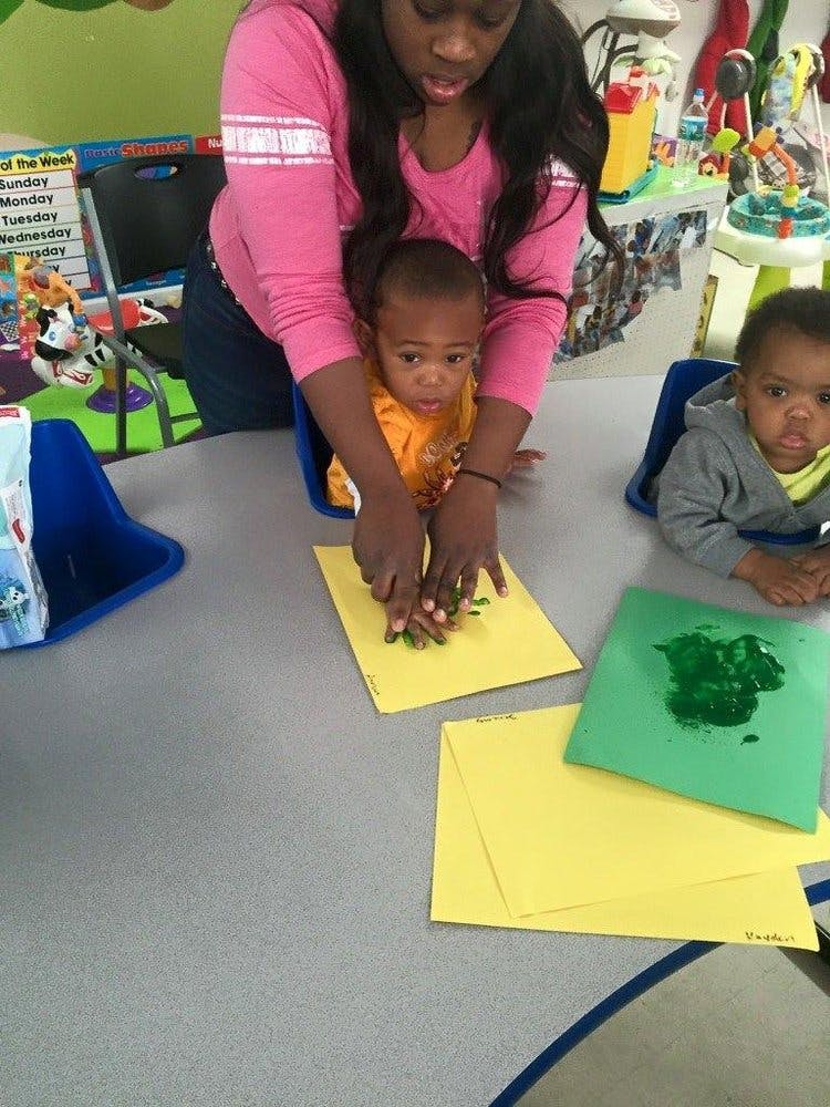 Person helping a child with finger painting on yellow paper