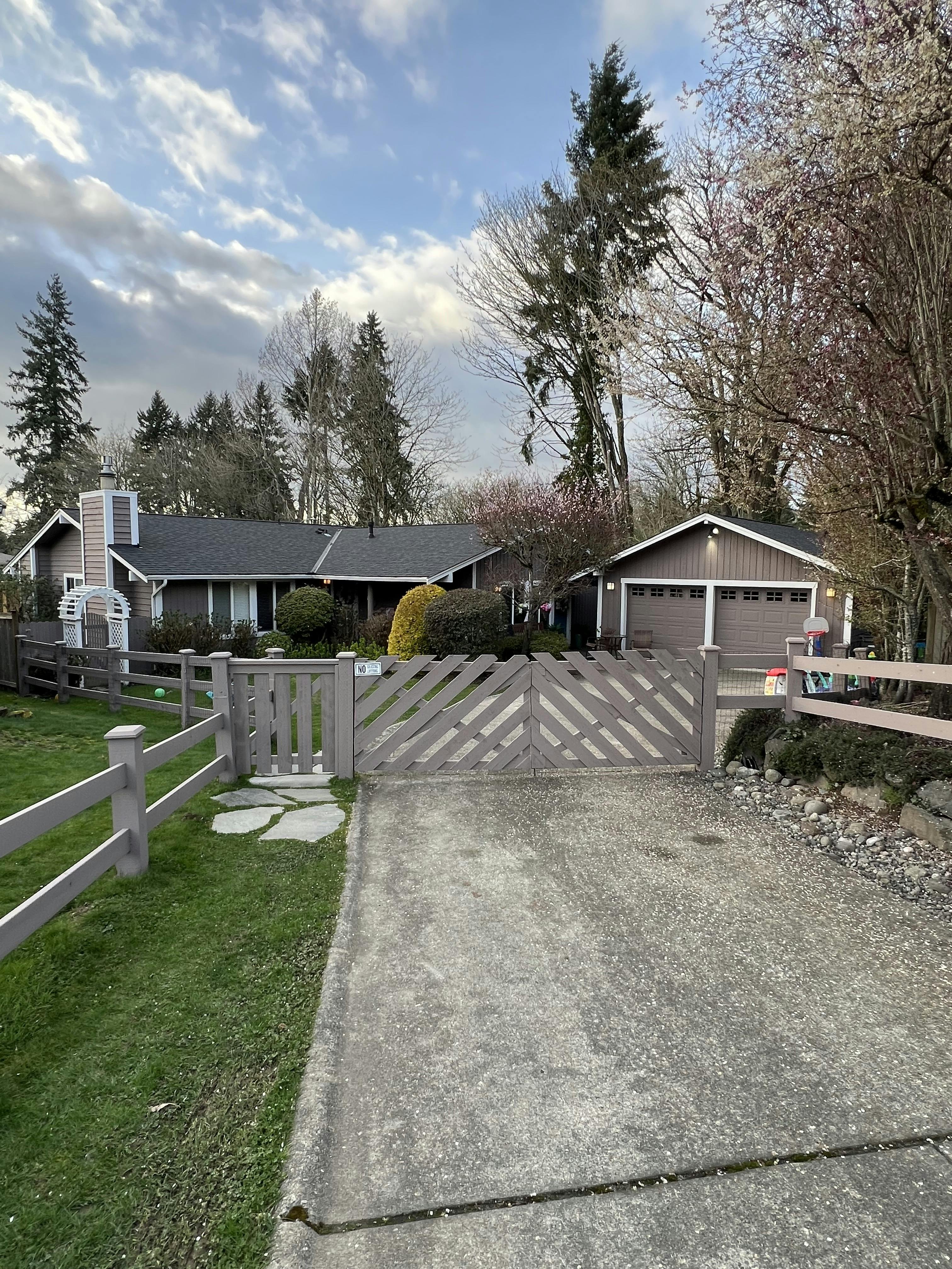 House with a brown fence and gated driveway, surrounded by trees and bushes