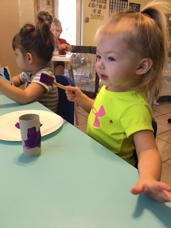 Child painting a cardboard tube at a table