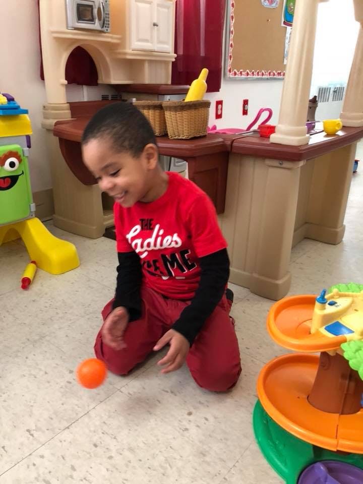Child kneeling on floor playing with an orange ball