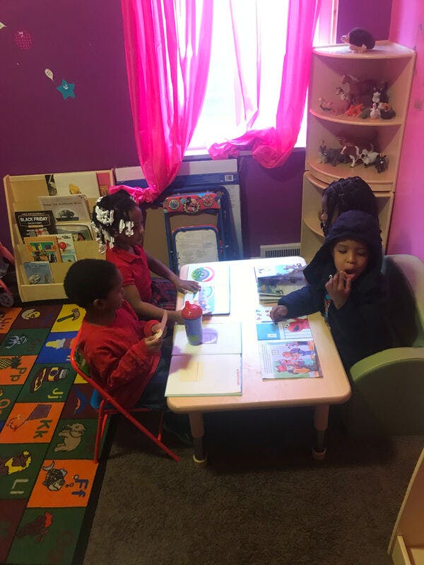 Three children sitting at a table with books in a classroom