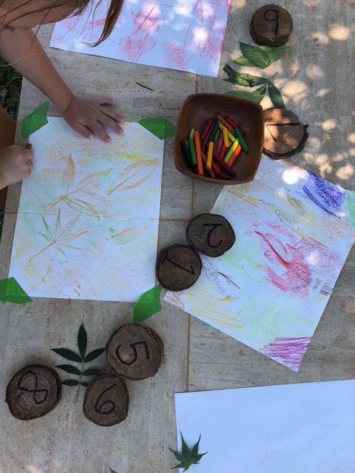 Child's hands on paper with leaf rubbings, crayons, and numbered wood slices