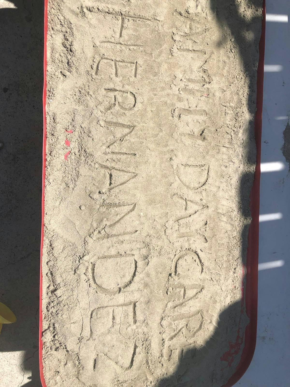 Text "MILDRED HERNANDEZ" written in sand