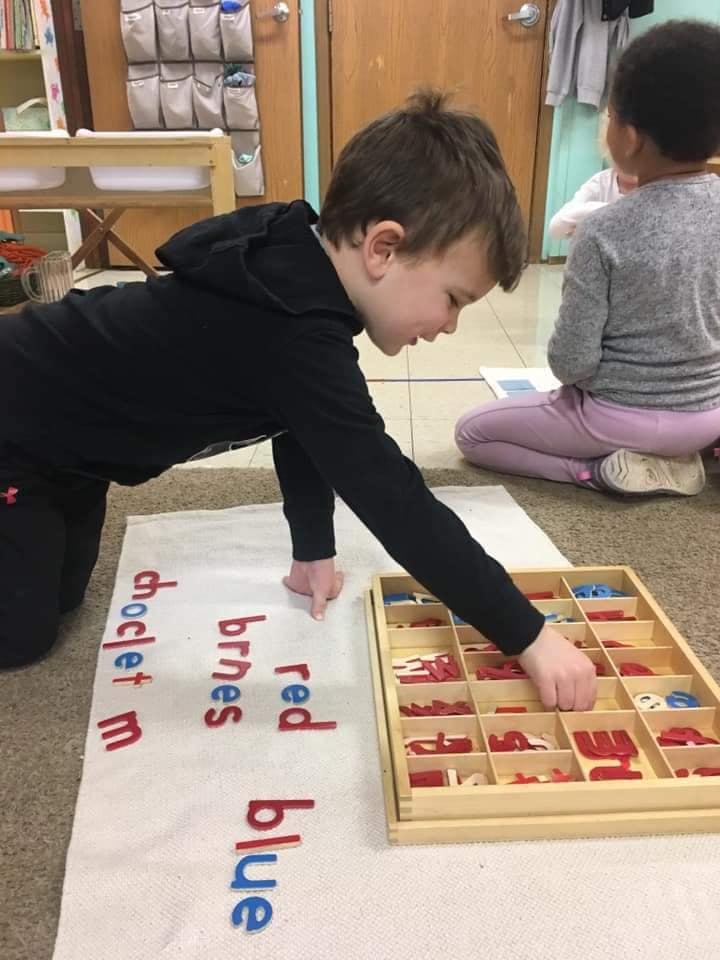 Child on floor placing letters on a mat with words like "blue" and "red"