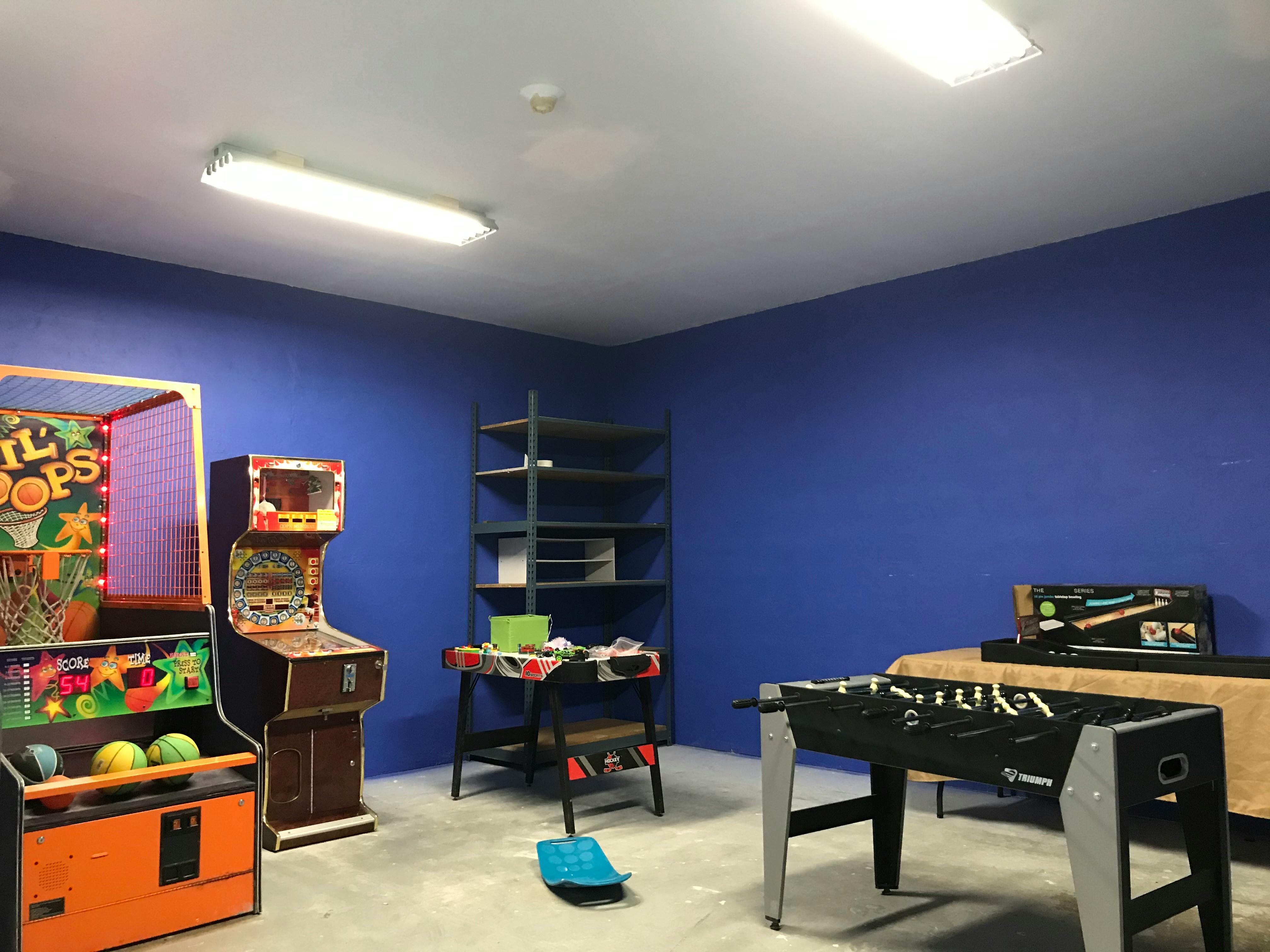 Arcade games, foosball table, and shelves in a room with blue walls