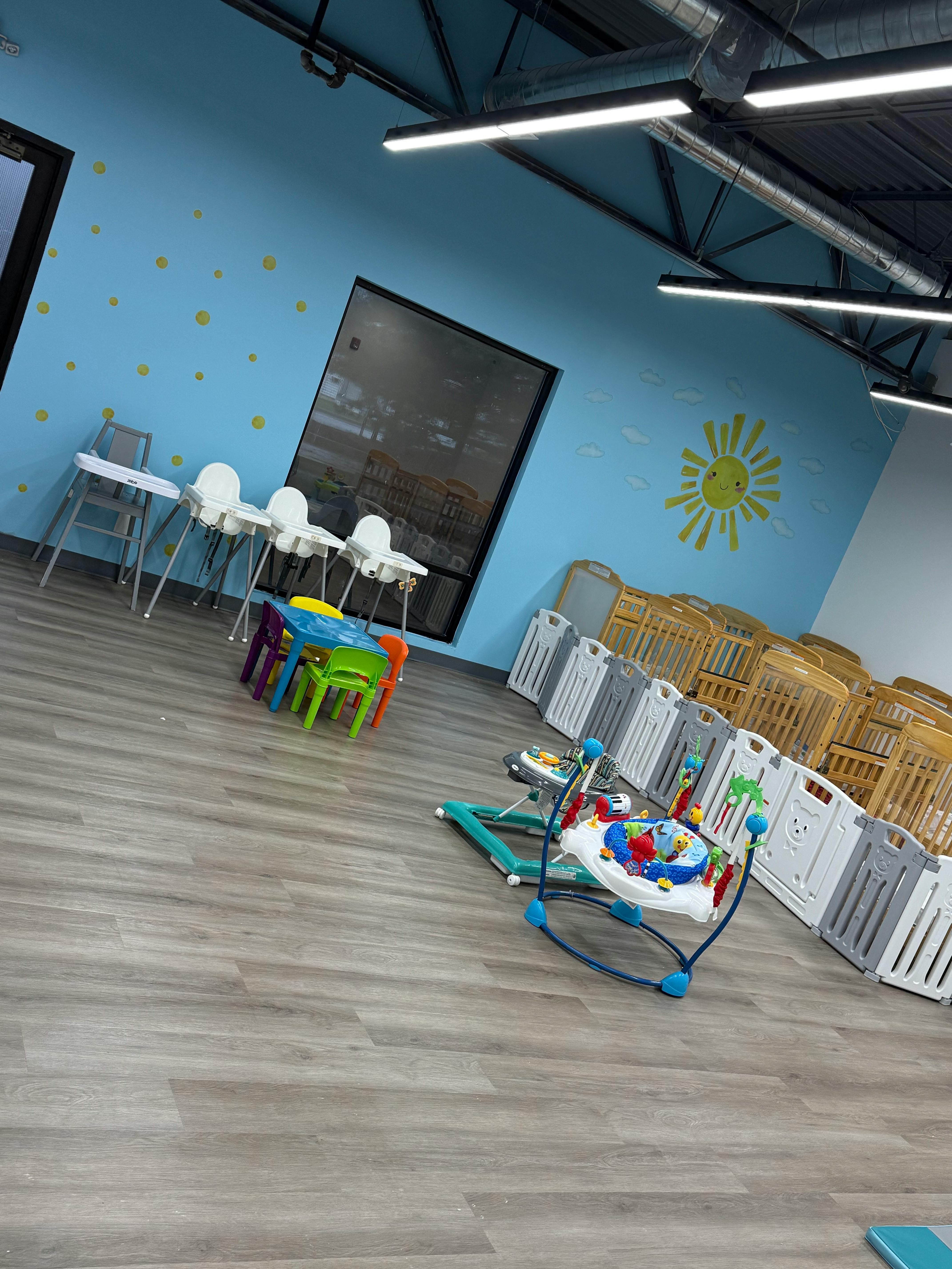 Playroom with high chairs, small table and chairs, baby bouncer, and cribs