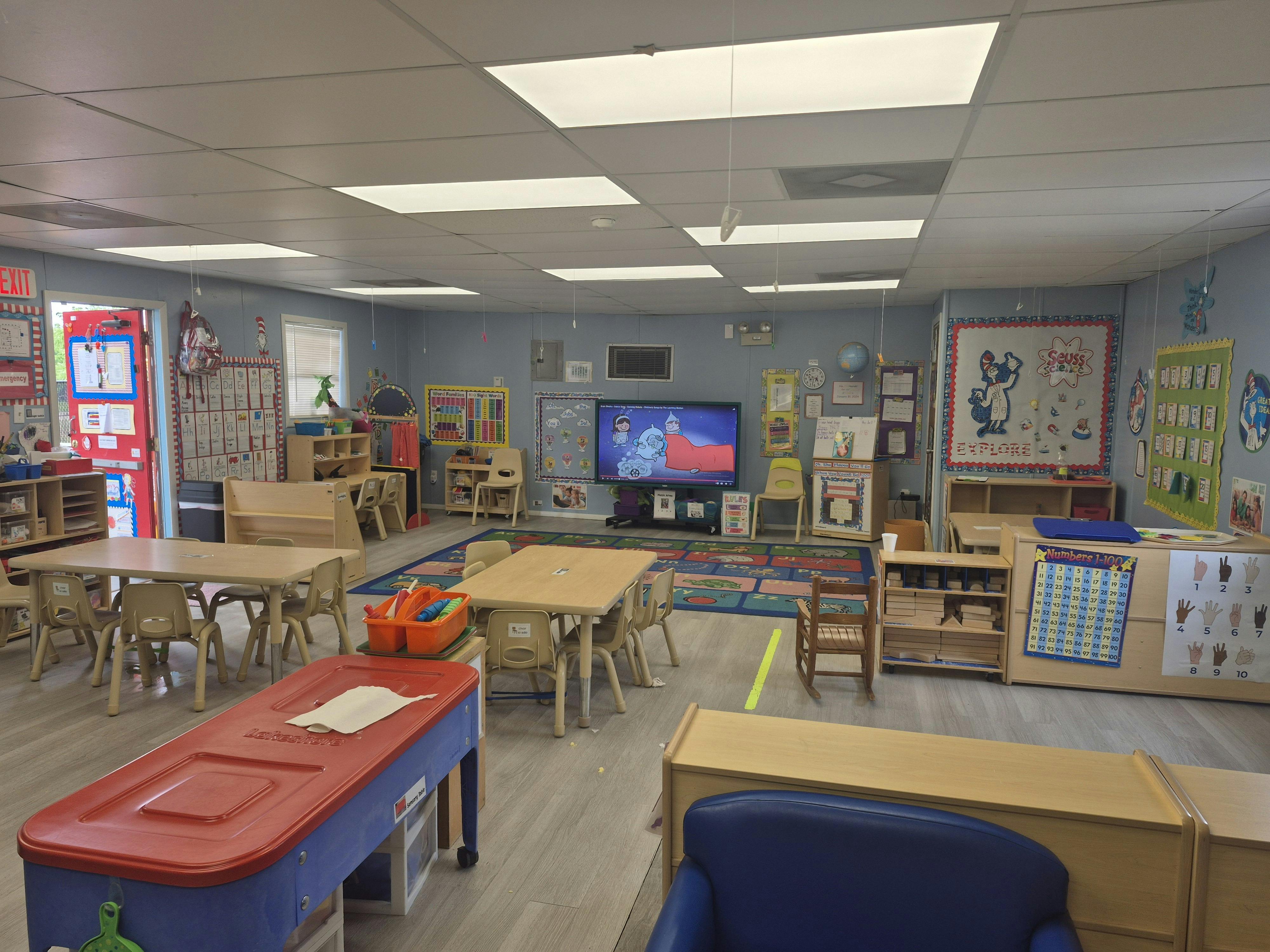 A classroom with small tables and chairs, a television, and various learning materials