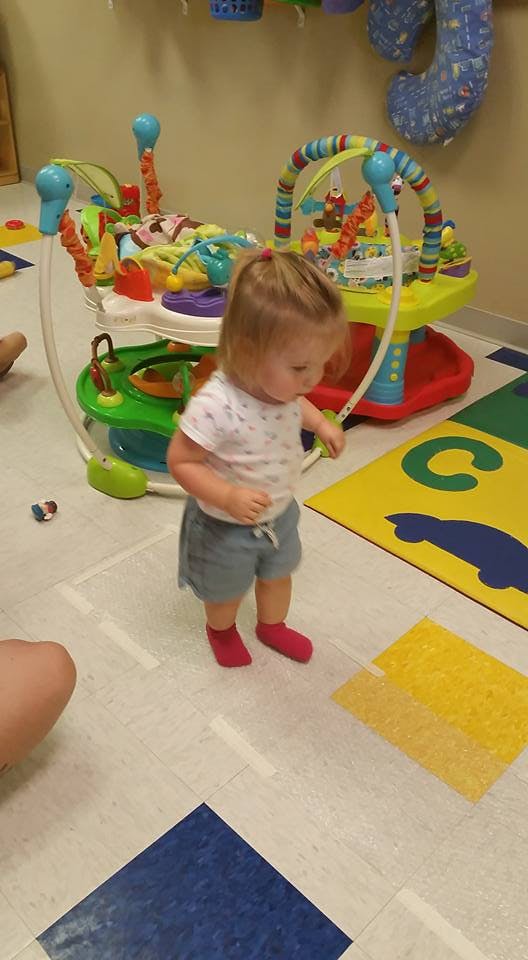Child standing in a room with a baby activity center
