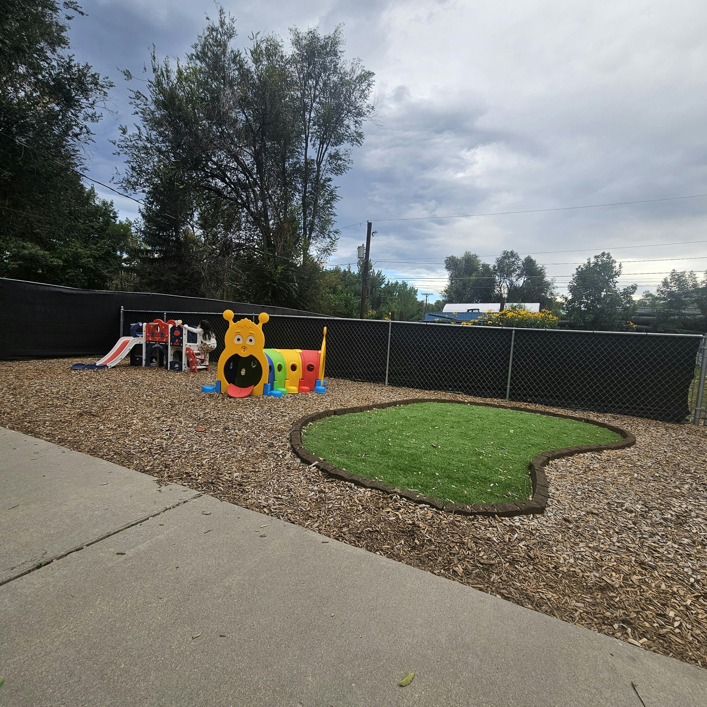 Outdoor play area with a slide, caterpillar tunnel, and small patch of grass