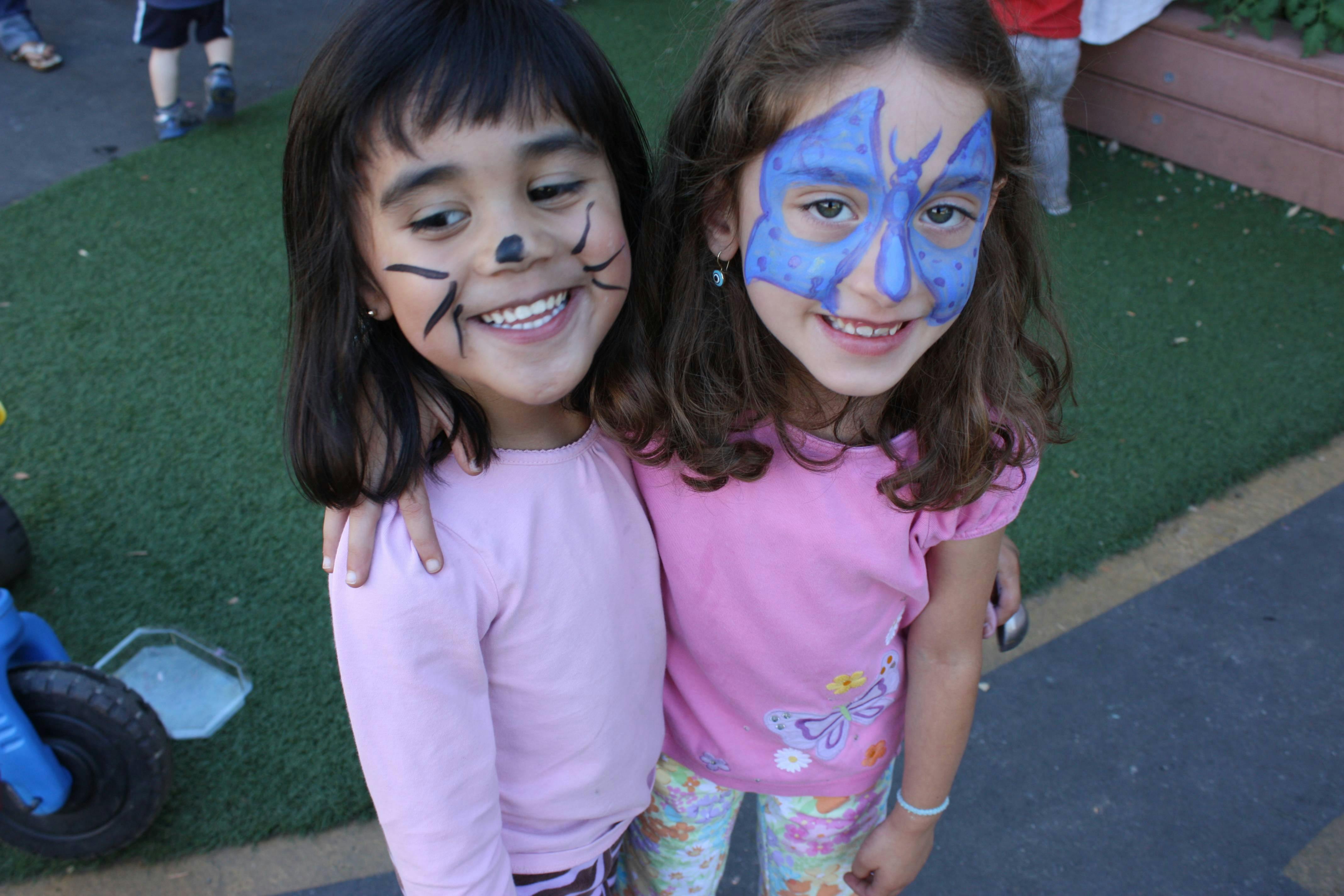 Two children with face paint, one with a cat face and one with a blue design