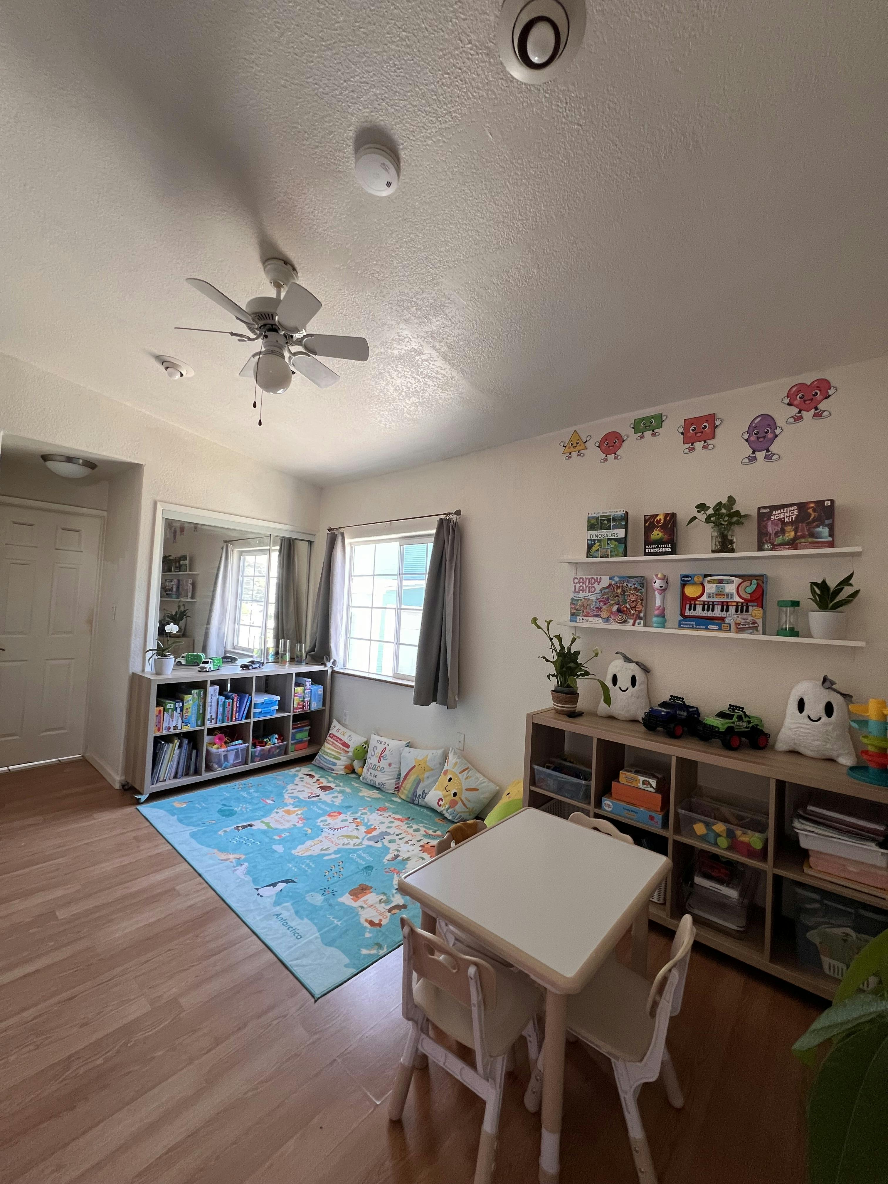 Child playroom with table, chairs, shelving units, and a world map floor mat