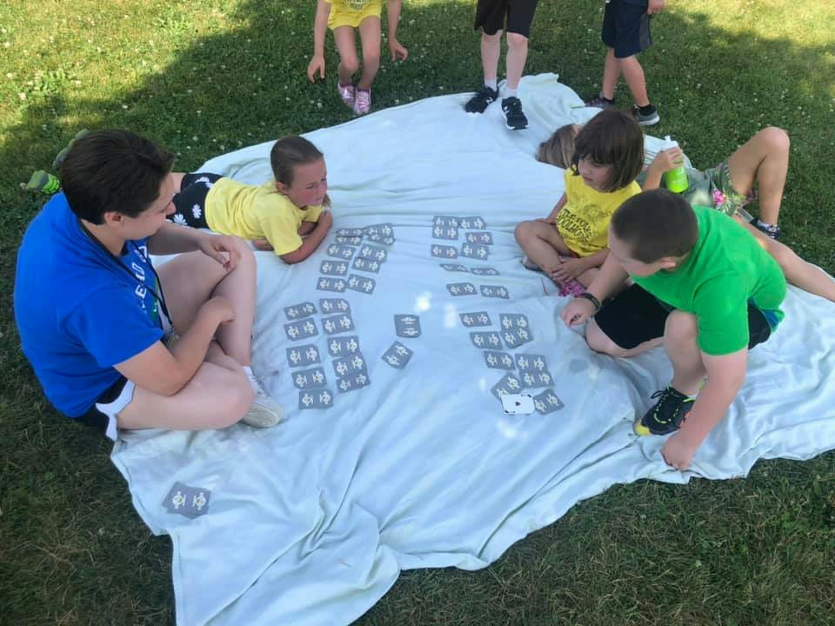 People and children playing a board game on a blanket outdoors