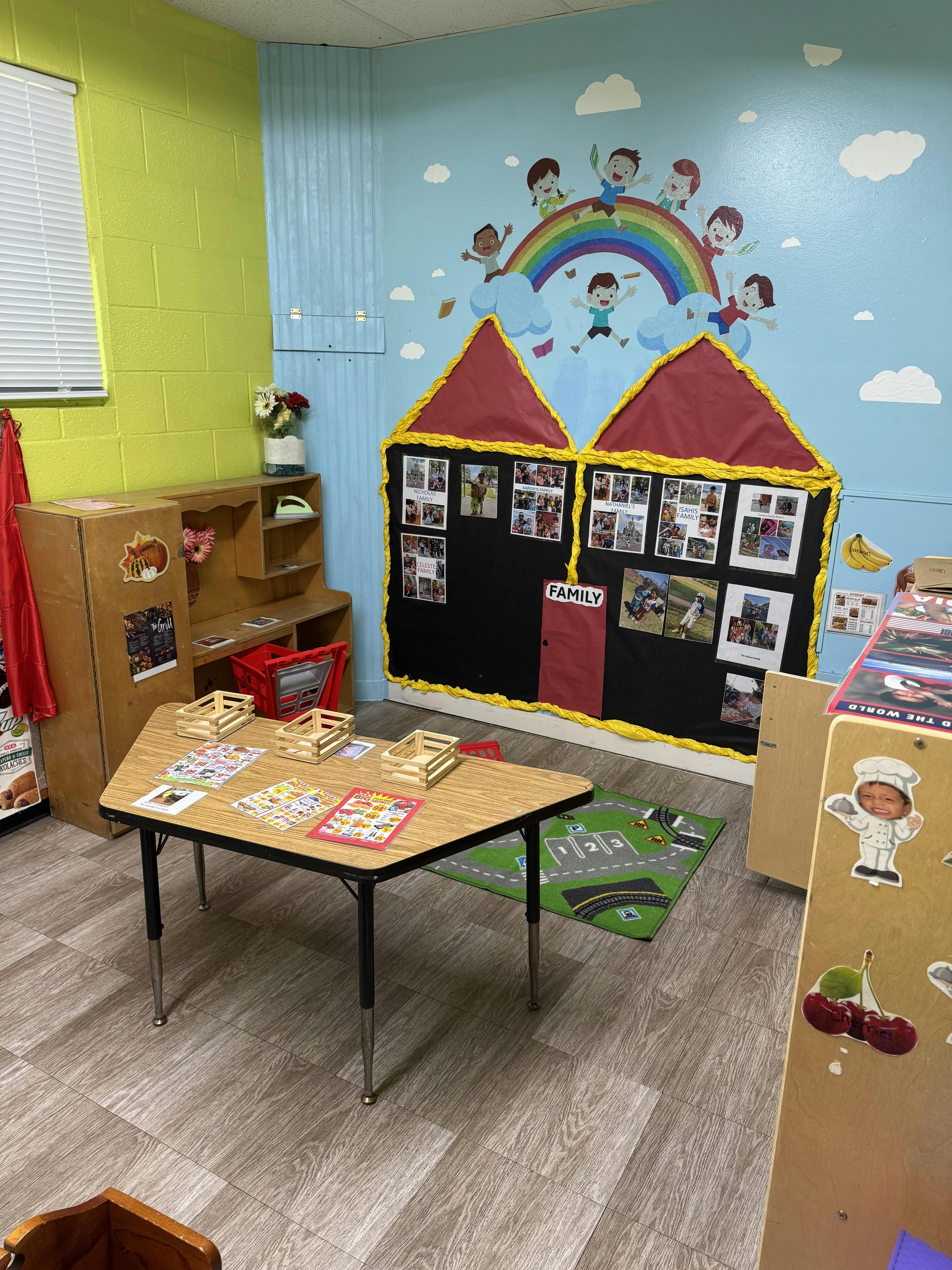 Classroom with a table, storage unit, and a wall decorated with a house and rainbow