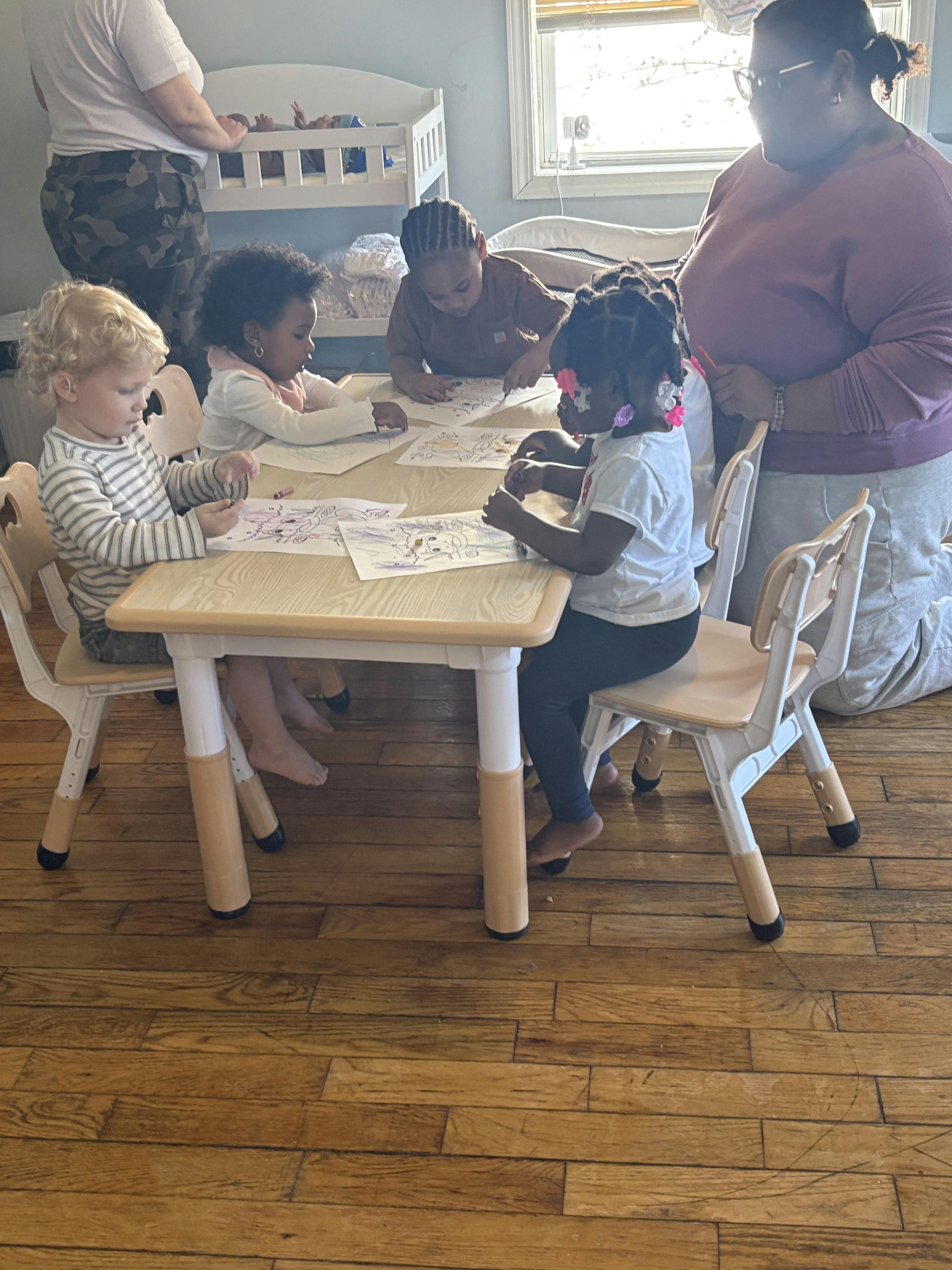 Children sitting at a table coloring on paper while adults supervise
