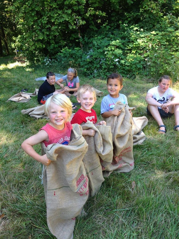Children in burlap sacks on grass with adults in a grassy area