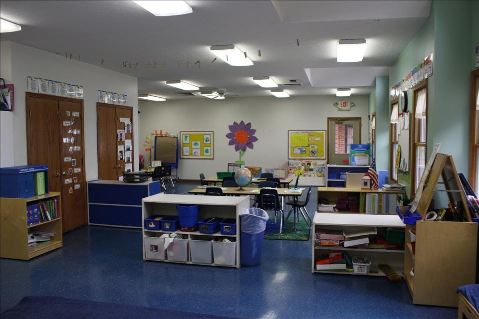 An empty classroom with tables, chairs, and shelves of educational materials