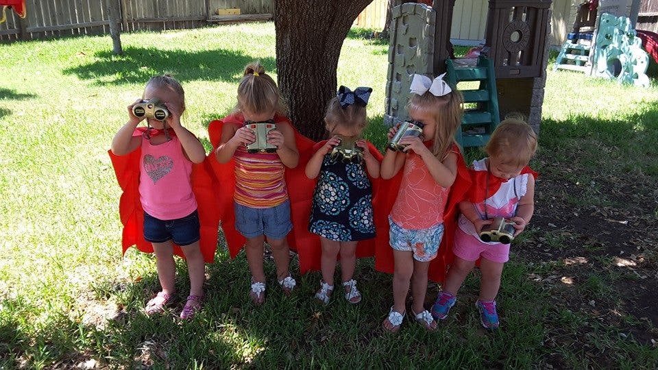 Five children wearing red capes and holding toy binoculars outdoors