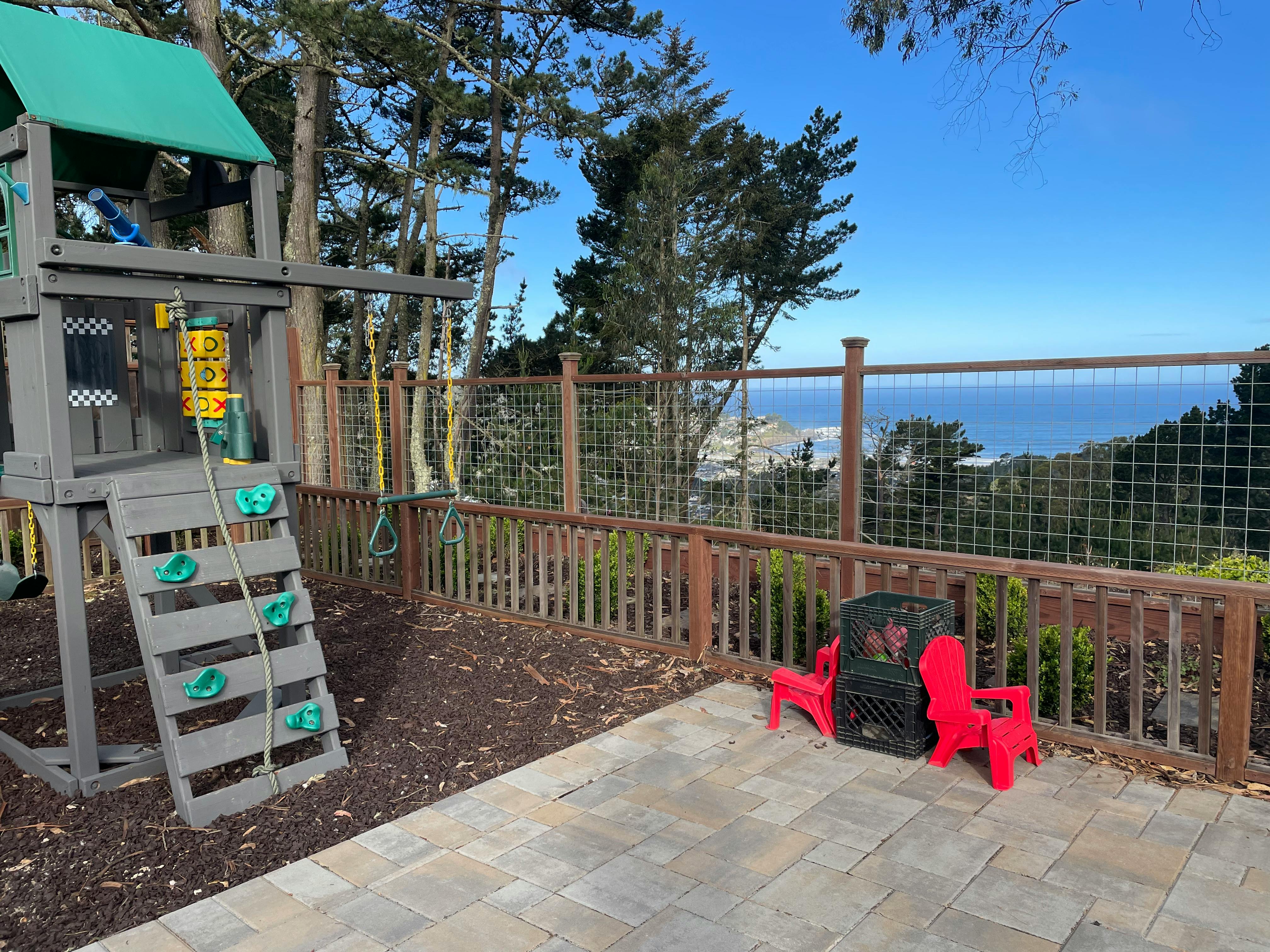 Play structure with slide and swings next to a patio overlooking the ocean