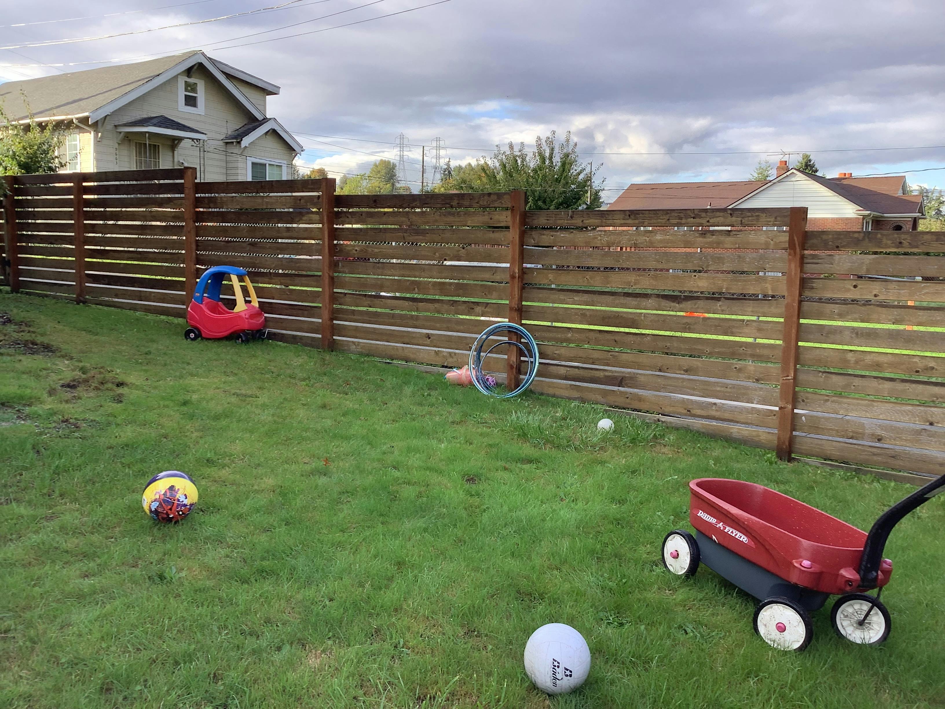 Backyard with a wooden fence, red wagon, and various balls on the grass