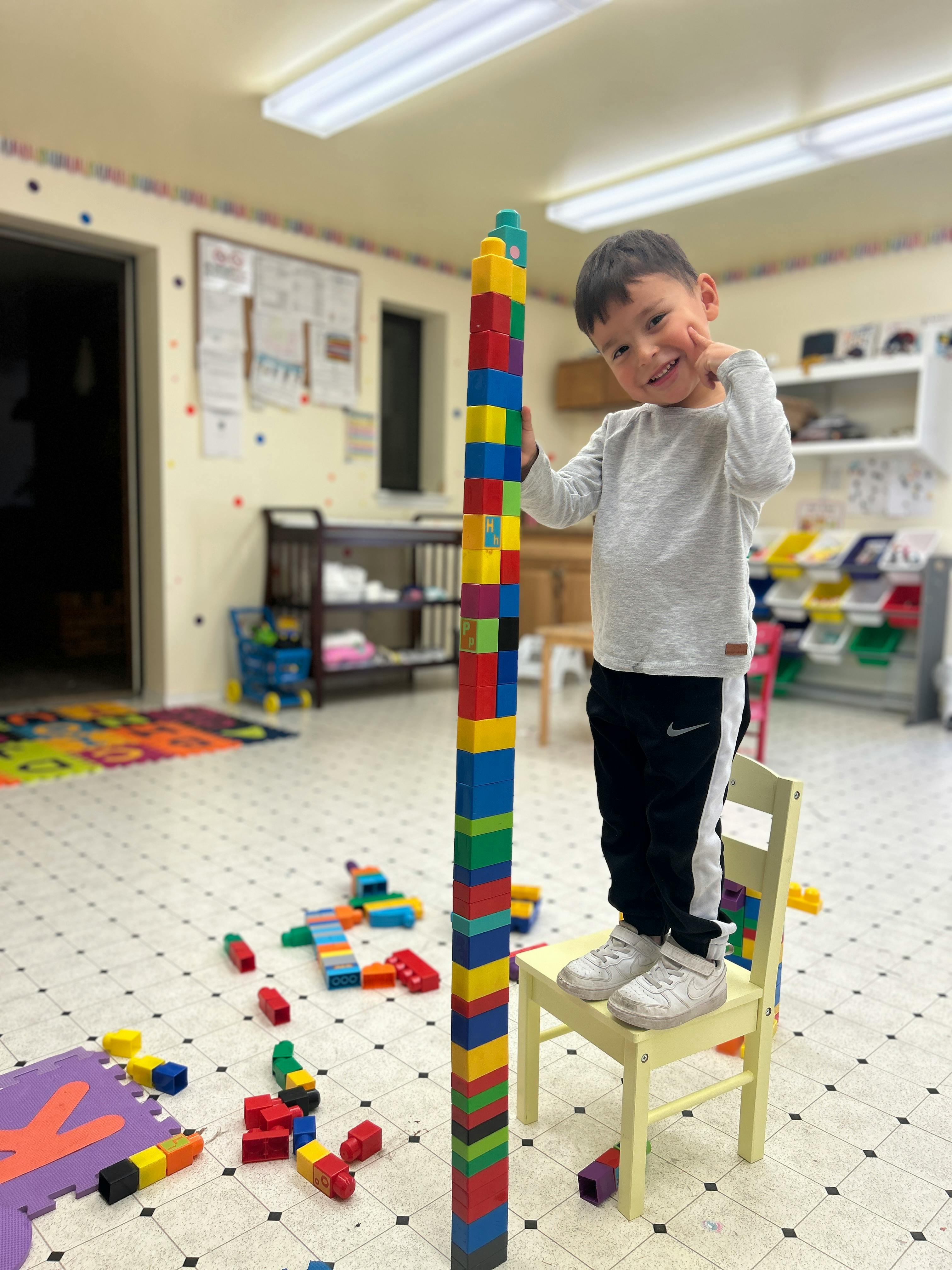 Child standing on a chair next to a tall tower of colorful blocks