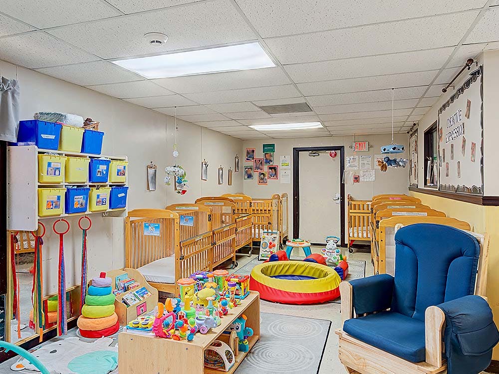 Cribs and toys in a childcare room with a blue rocking chair