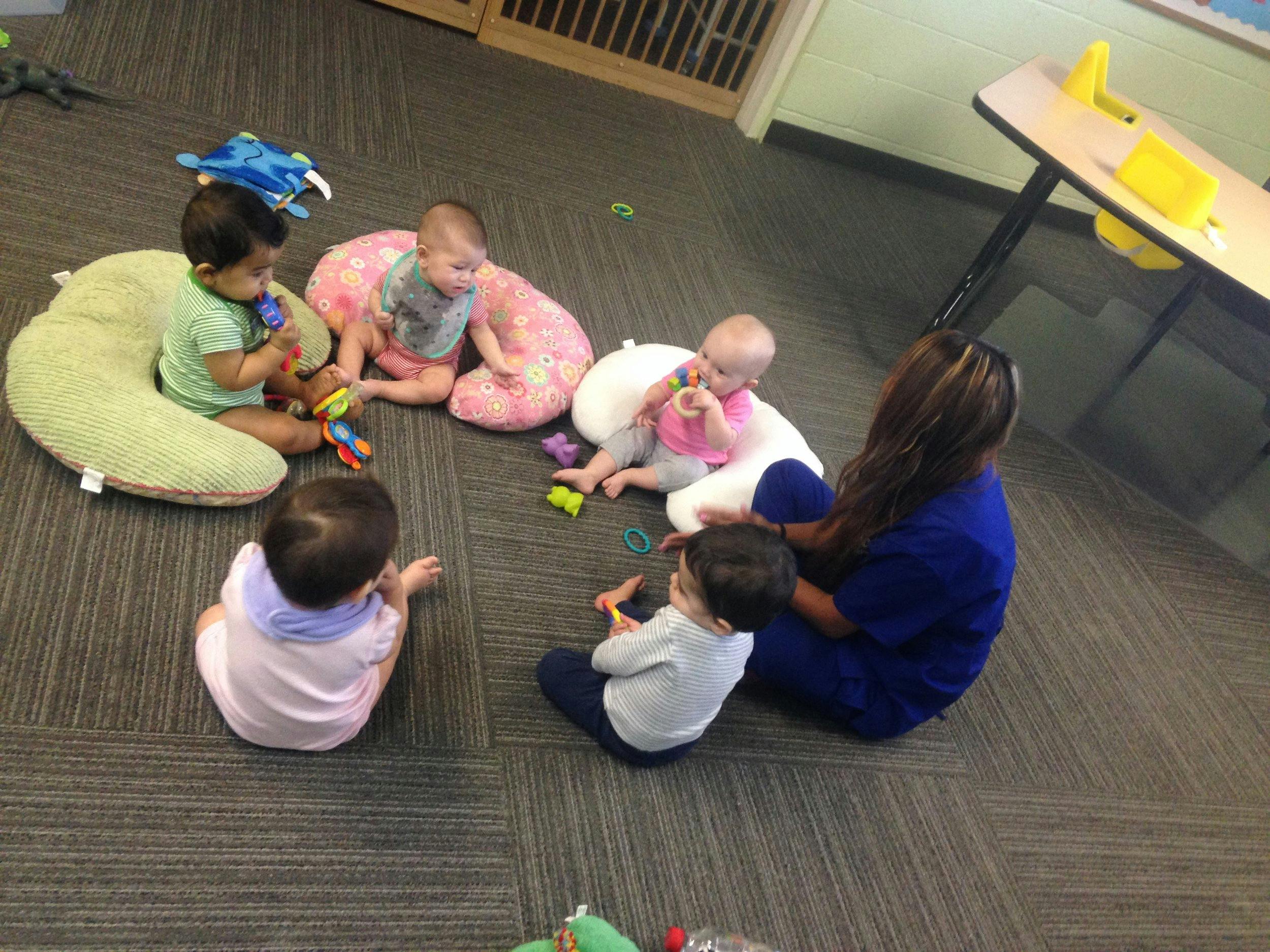 Adult and multiple babies sitting on the floor playing with toys