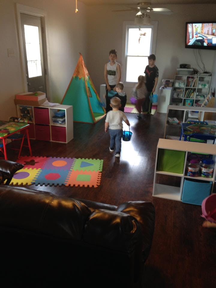 Child walking with a bucket in a room with other people and a play tent