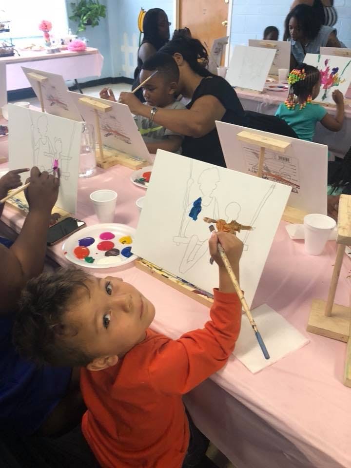 Child painting on an easel at a table with other people painting