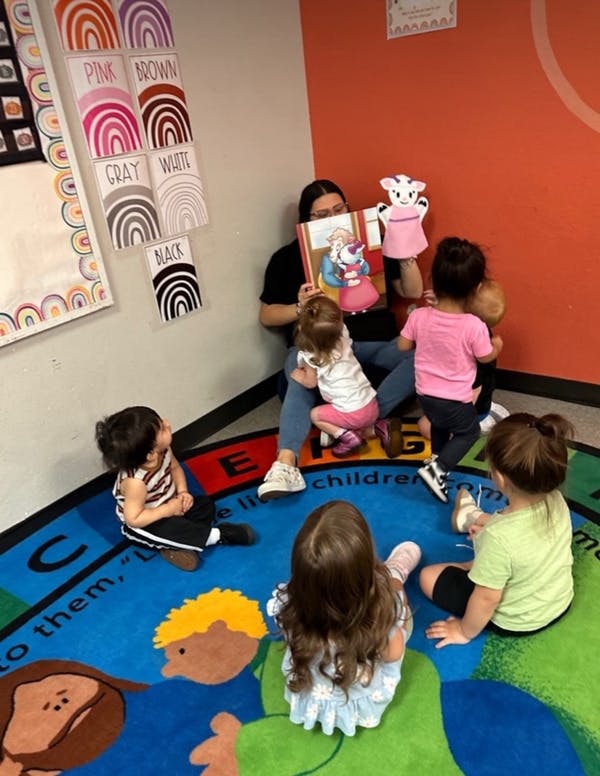 Person reading a book to children sitting on a colorful rug