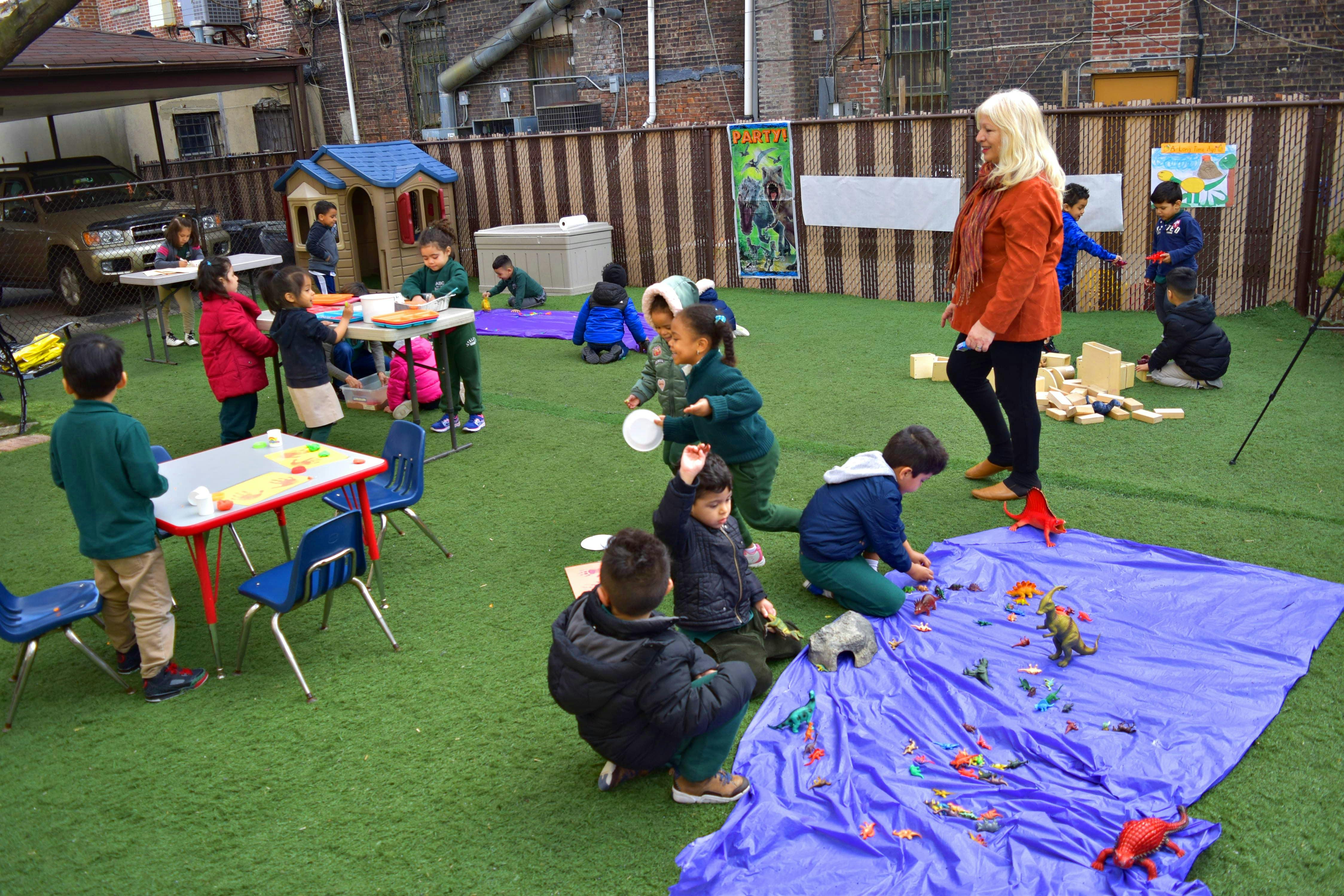 Adult and children playing outdoors with toys and tables